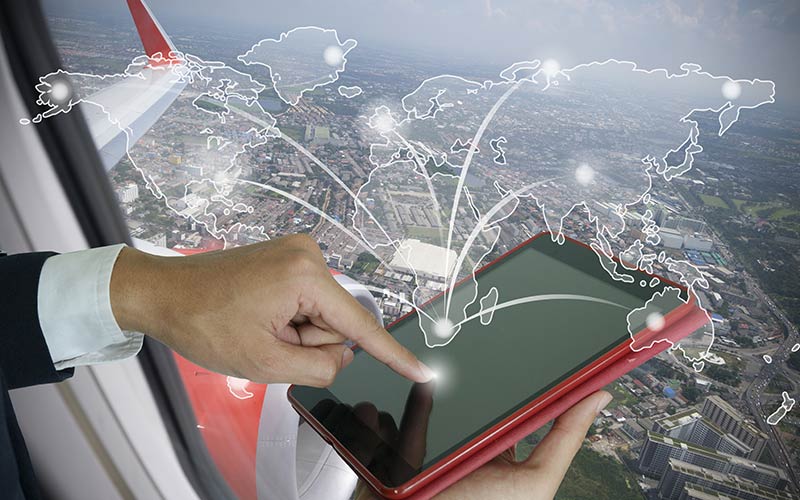 Photo of a man in an airplane touching a tablet with overlaying continents and connecting lines